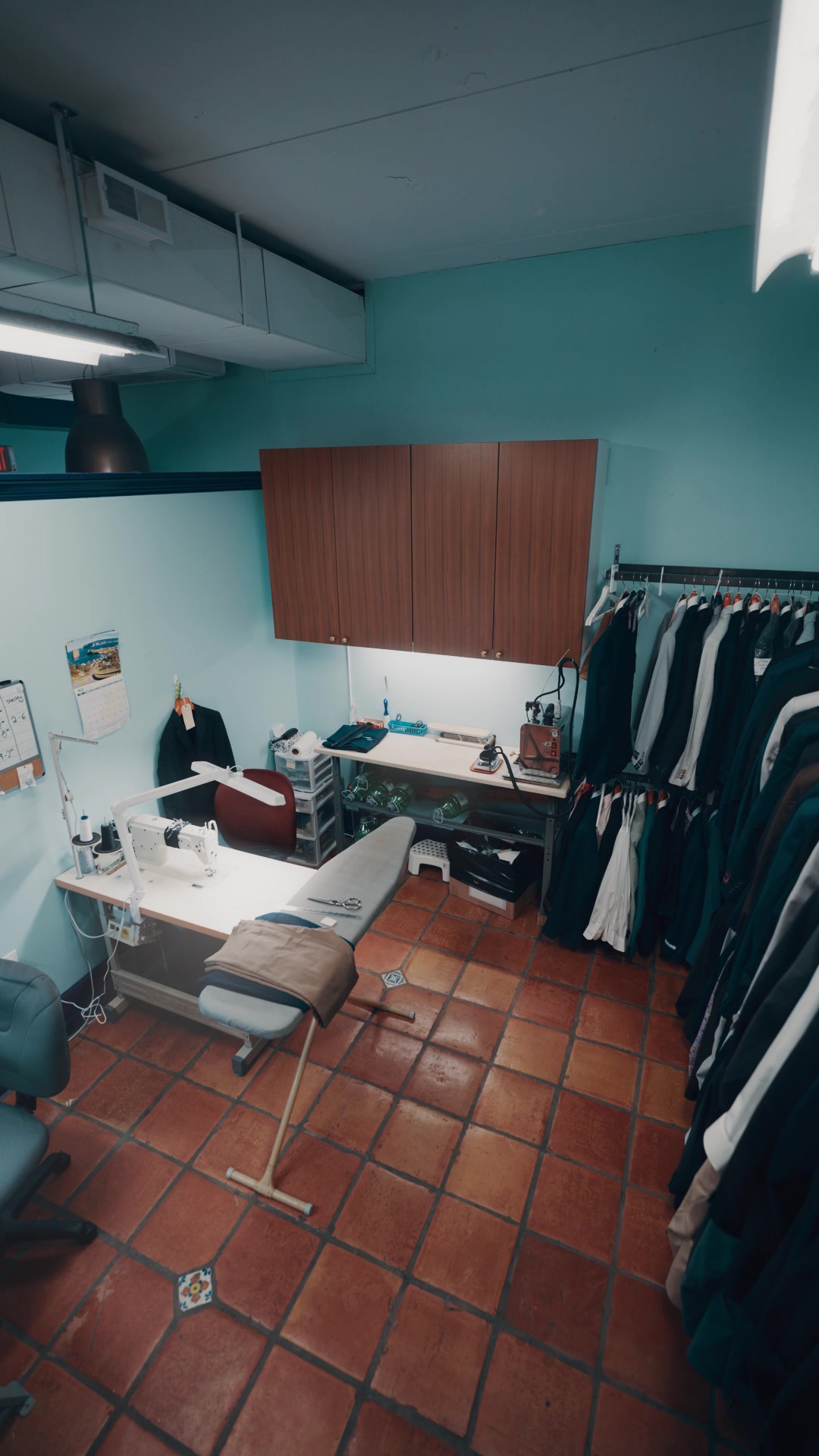 In-house tailor shop with sewing machine, press, and garments on the rail